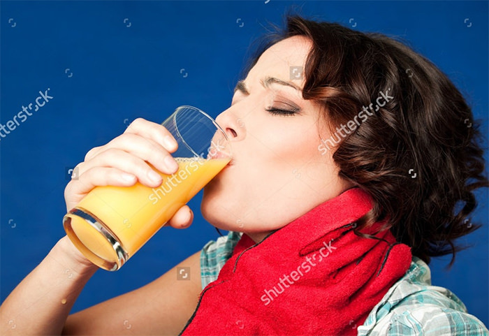 Young woman drinking orange juice in pain while being strangled by the throat