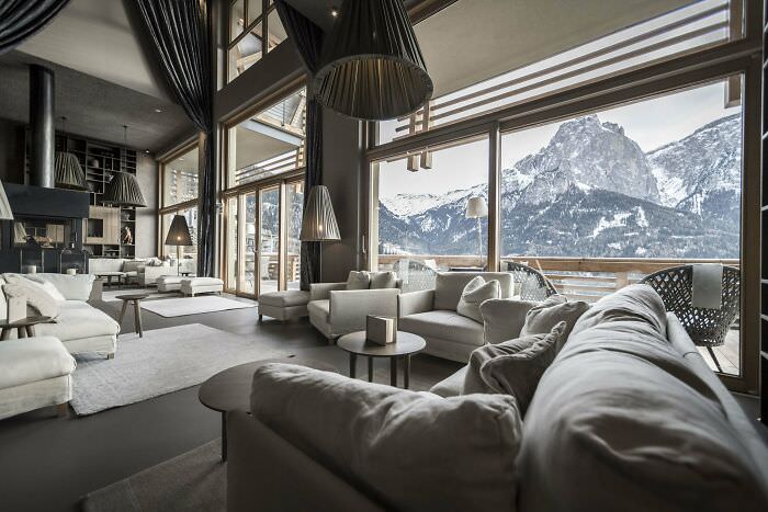 A tall and spacious hotel lounge centered around a fireplace with stunning views of the Italian Dolomites in South Tyrol, Northern Italy