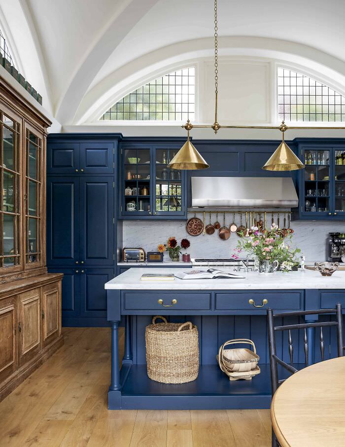 A blue cabinetry kitchen with a vaulted ceiling and arched clerestory windows in a 1910s Arts and Crafts-styled house in North London, UK