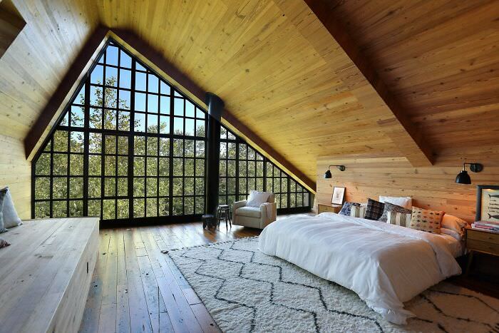 A spacious attic bedroom with a giant window under a vaulted ceiling in Bridgehampton, South Fork, Suffolk County, Long Island, New York.