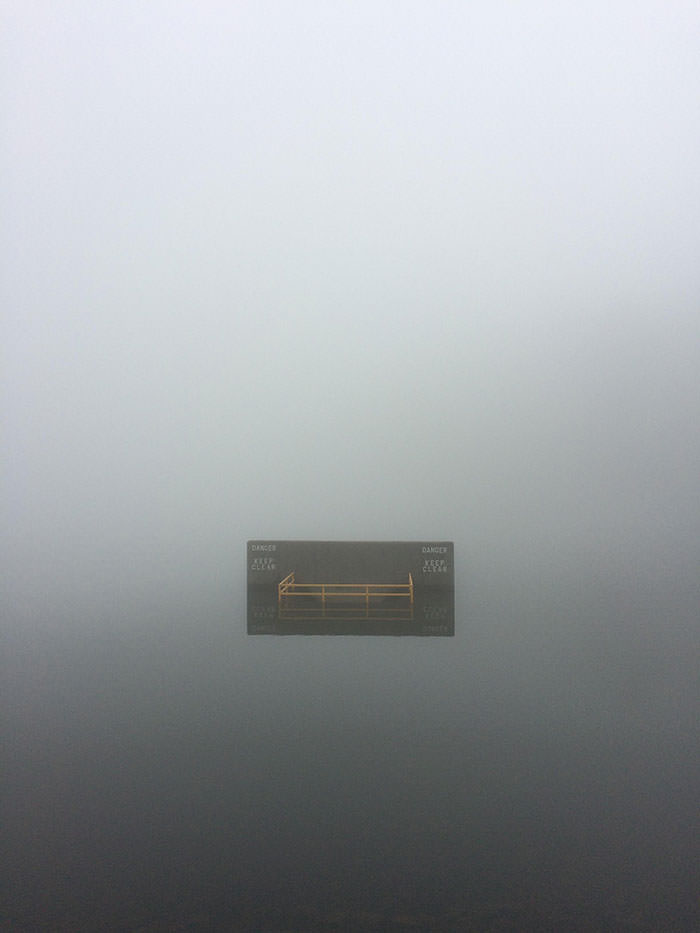 Fog over a lake that makes a warning sign look like it is surrounded by nothingness.