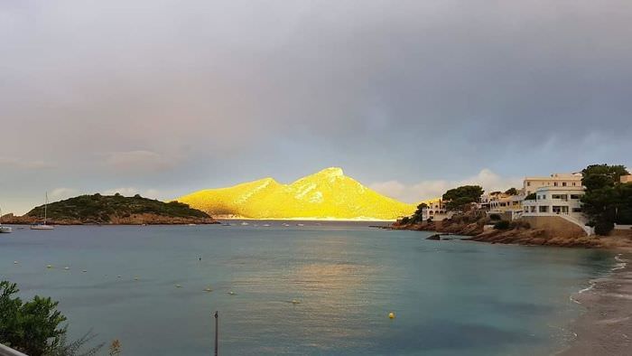 A small island off the coast caught by the sun during a stormy day in Mallorca, Spain.