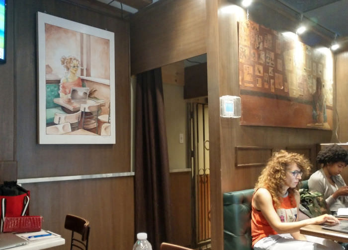 This woman at a cafe really resembles the woman in the painting right behind her.
